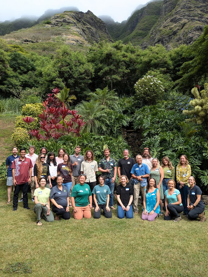 Group of people posing for a photo in a lush green outdoor setting with mountains in the background.